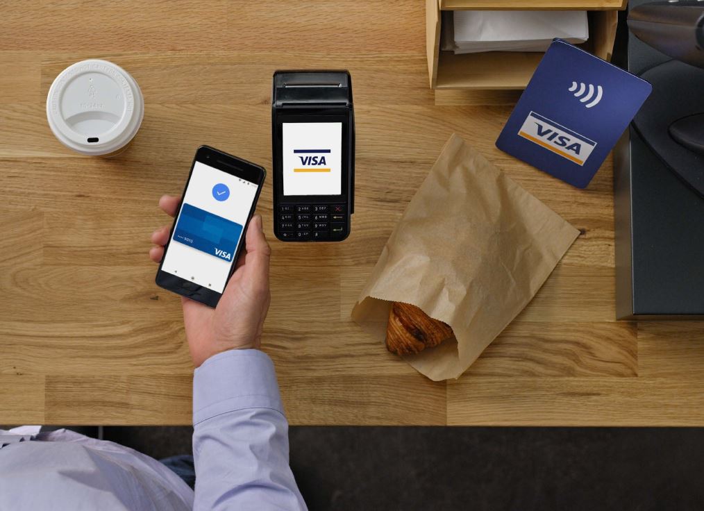 man holding phone near contactless card reader in coffee shop